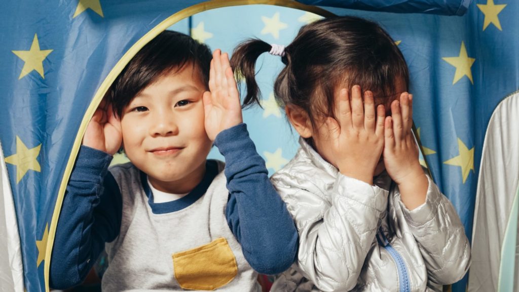 two young children playing peek a boo with hands