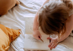 young child drawing in notebook laying on bed