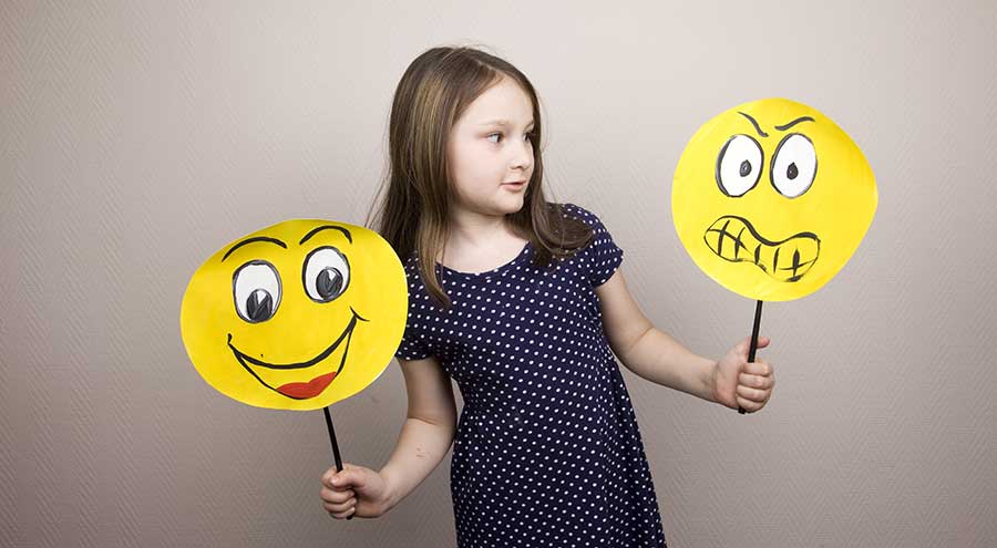 social emotional learning young girl holding up homemade smiley and angry face yellow construction cutout