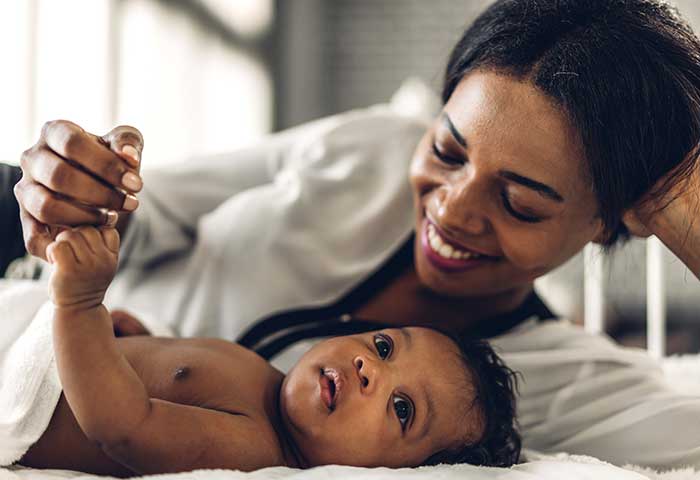 black or brown mom smiling at infant laying down